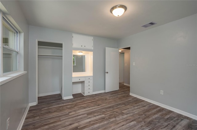 unfurnished bedroom featuring dark wood-type flooring, built in desk, and a closet