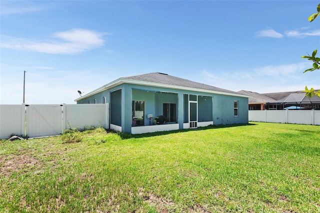 back of house with a fenced backyard, a gate, a lawn, and stucco siding