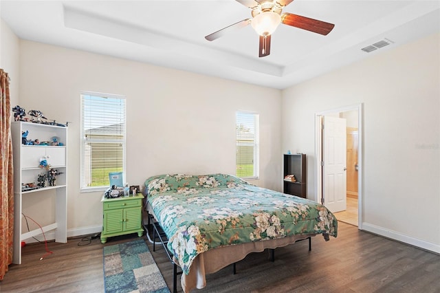 bedroom featuring a raised ceiling, visible vents, ceiling fan, wood finished floors, and baseboards