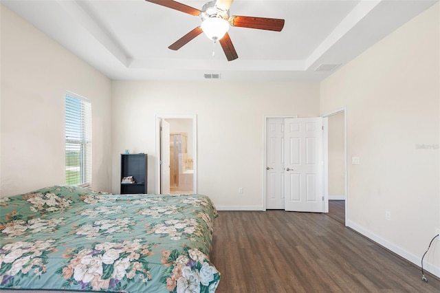 bedroom with baseboards, visible vents, a tray ceiling, and dark wood-type flooring