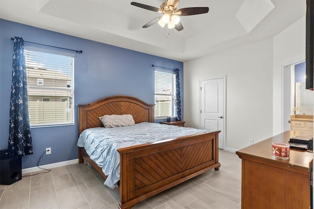 bedroom featuring a tray ceiling, ensuite bath, and ceiling fan