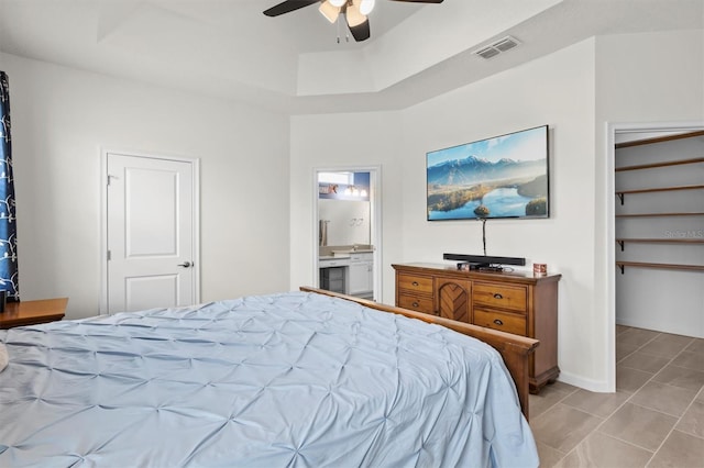 bedroom with a tray ceiling, ensuite bath, and ceiling fan