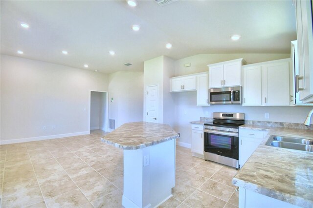 kitchen with appliances with stainless steel finishes, white cabinets, vaulted ceiling, sink, and a center island