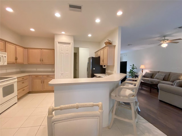 kitchen with light brown cabinetry, a breakfast bar area, ceiling fan, kitchen peninsula, and white appliances