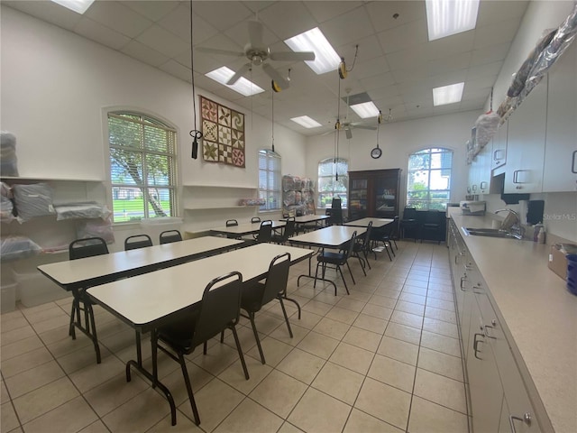 tiled dining space with ceiling fan, sink, a high ceiling, and a drop ceiling