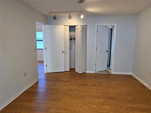 unfurnished bedroom with two closets, wood-type flooring, rail lighting, and a textured ceiling