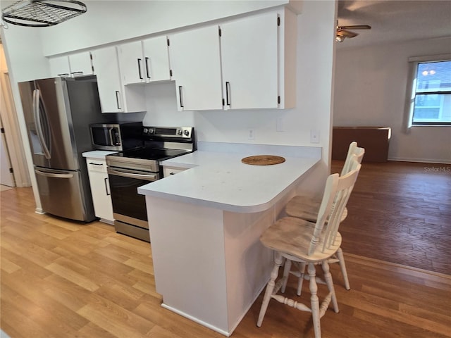 kitchen featuring light wood-type flooring, appliances with stainless steel finishes, kitchen peninsula, ceiling fan, and white cabinets