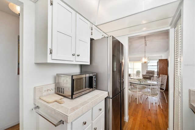 kitchen with white cabinets, light wood-type flooring, hanging light fixtures, and tile countertops