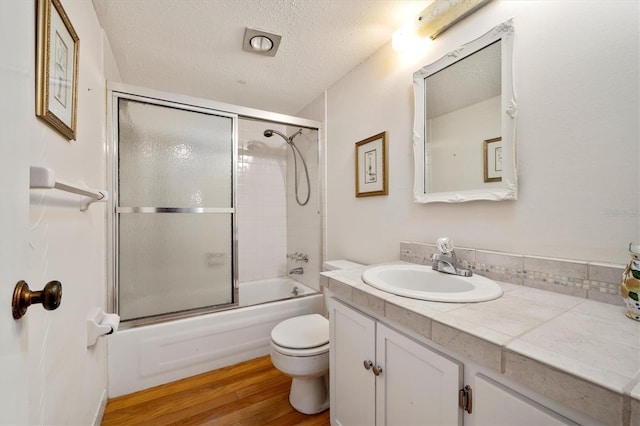 full bathroom with enclosed tub / shower combo, wood-type flooring, a textured ceiling, toilet, and vanity