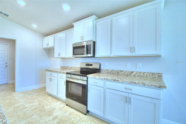 kitchen with appliances with stainless steel finishes, white cabinets, vaulted ceiling, light tile patterned floors, and light stone countertops