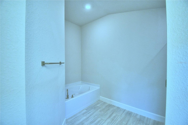 bathroom with vaulted ceiling, wood-type flooring, and a bath