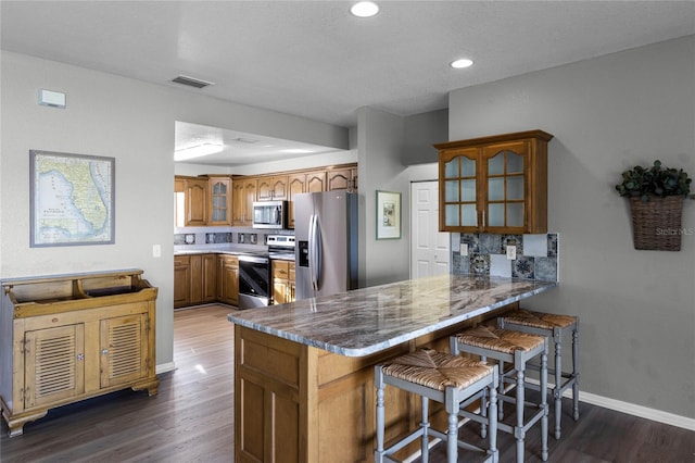 kitchen with a kitchen breakfast bar, dark hardwood / wood-style flooring, kitchen peninsula, a textured ceiling, and appliances with stainless steel finishes