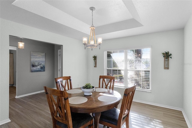 dining space with a textured ceiling, hardwood / wood-style flooring, a raised ceiling, and a notable chandelier