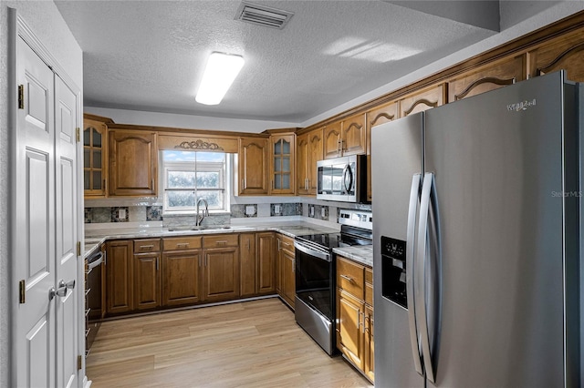 kitchen featuring sink, light hardwood / wood-style flooring, light stone countertops, a textured ceiling, and stainless steel appliances