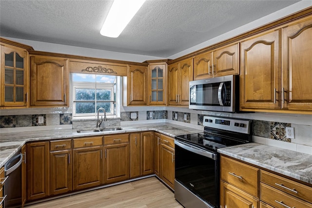 kitchen with light stone countertops, sink, stainless steel appliances, tasteful backsplash, and light hardwood / wood-style floors