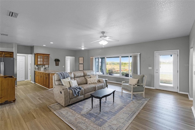 living room featuring ceiling fan, light hardwood / wood-style floors, and a textured ceiling