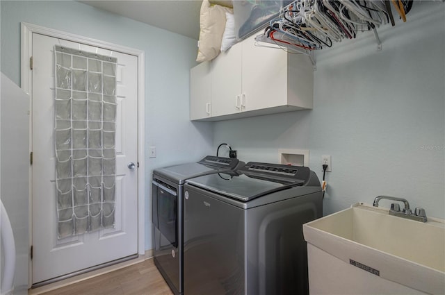 laundry area with cabinets, light wood-type flooring, washing machine and clothes dryer, and sink