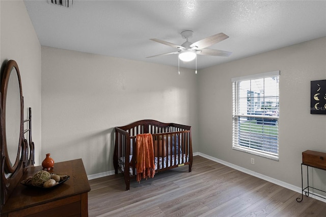 bedroom with ceiling fan, a nursery area, and light wood-type flooring