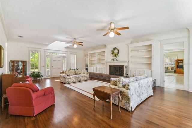 living room with built in features, a brick fireplace, tile patterned floors, ceiling fan, and ornamental molding