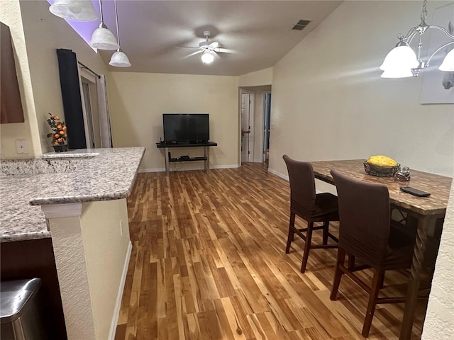 dining area featuring ceiling fan with notable chandelier, hardwood / wood-style flooring, and vaulted ceiling