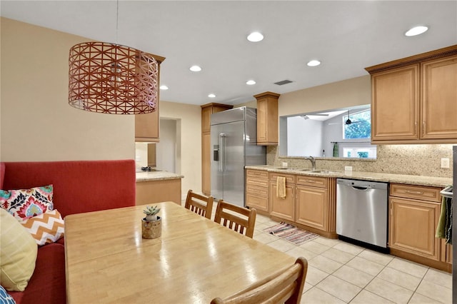 kitchen featuring light stone countertops, appliances with stainless steel finishes, light tile patterned floors, decorative backsplash, and sink