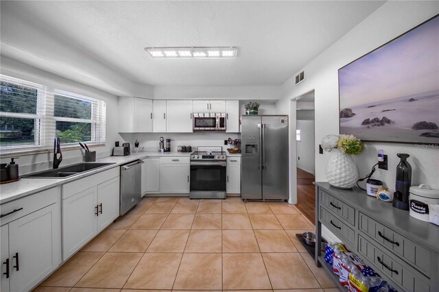 kitchen featuring appliances with stainless steel finishes, light tile patterned floors, white cabinets, and sink