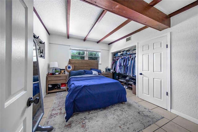 bedroom with beamed ceiling, tile patterned flooring, a closet, and a textured ceiling