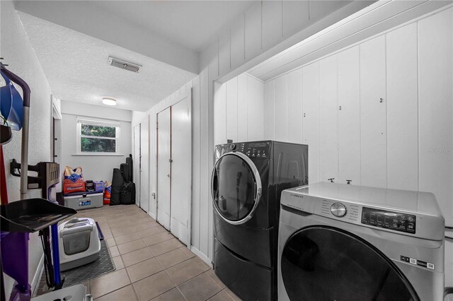 laundry area with washing machine and dryer, a textured ceiling, and light tile patterned floors