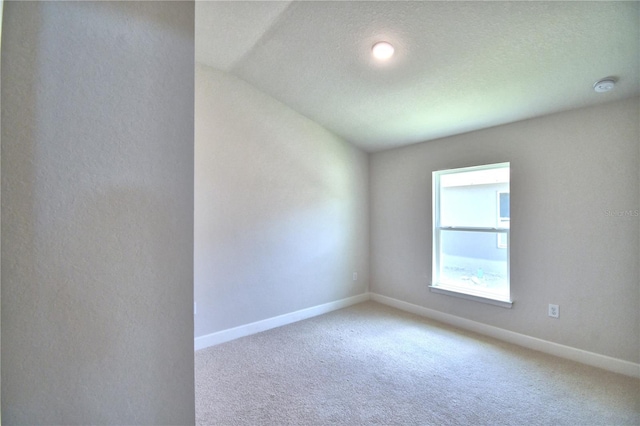 spare room with carpet, a textured ceiling, and vaulted ceiling