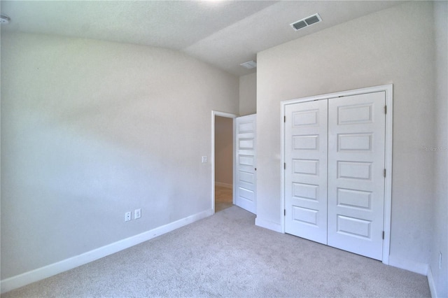 unfurnished bedroom featuring light carpet, a closet, and lofted ceiling