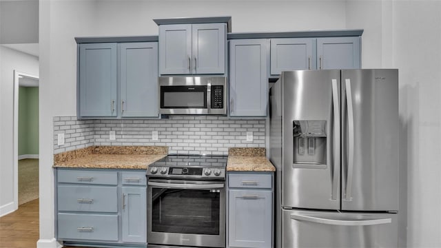 kitchen featuring stainless steel appliances, tasteful backsplash, wood finished floors, and light stone countertops