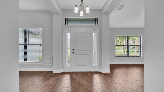 foyer with baseboards, visible vents, a chandelier, and wood finished floors