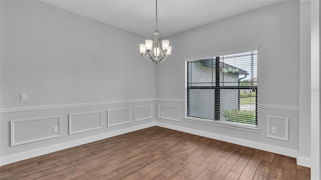 unfurnished room featuring a wealth of natural light, an inviting chandelier, and wood finished floors