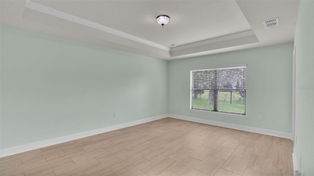 empty room featuring light wood-style flooring, visible vents, baseboards, and a raised ceiling