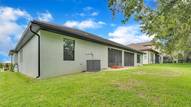 rear view of house with cooling unit, stucco siding, a lawn, and fence