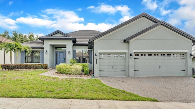 ranch-style home featuring a tiled roof, an attached garage, decorative driveway, a front yard, and stucco siding