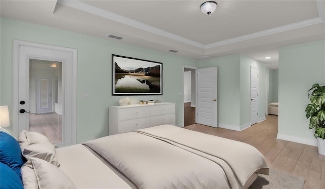 bedroom with a raised ceiling, light wood-type flooring, crown molding, and ensuite bathroom