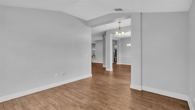 unfurnished room with a notable chandelier, lofted ceiling, visible vents, wood finished floors, and baseboards