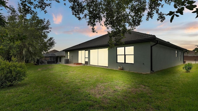 rear view of property featuring cooling unit, a yard, and stucco siding