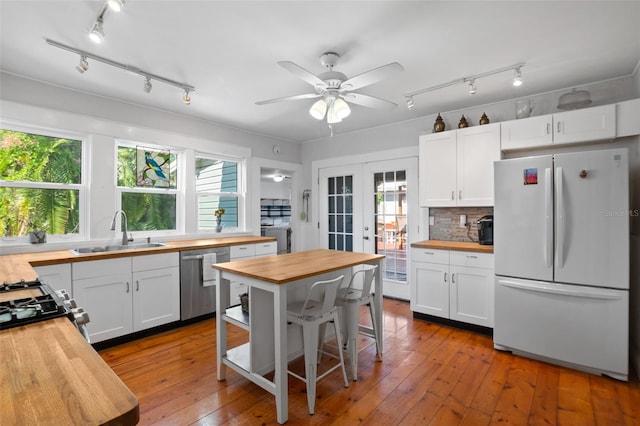 kitchen with butcher block countertops, sink, white cabinetry, stainless steel dishwasher, and white fridge