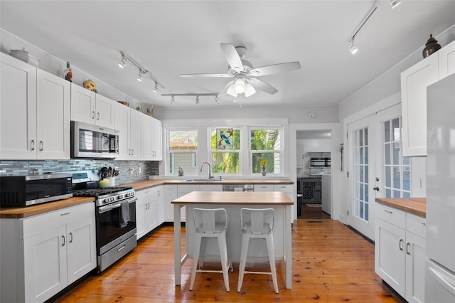 kitchen with a breakfast bar area, wooden counters, stainless steel appliances, a center island, and white cabinets