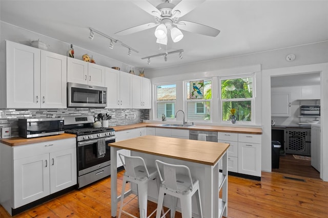 kitchen featuring stainless steel appliances, light wood-type flooring, sink, butcher block countertops, and track lighting