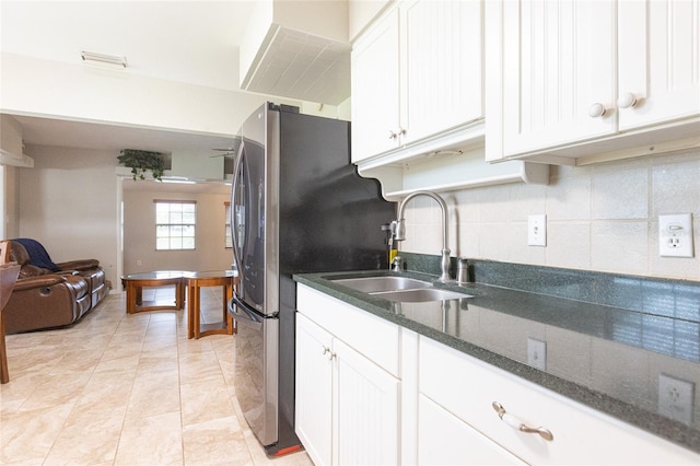 kitchen featuring sink, white cabinetry, dark stone counters, decorative backsplash, and stainless steel refrigerator