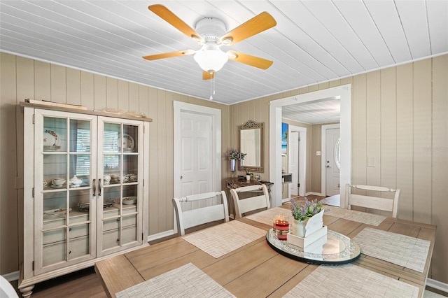 dining space with ceiling fan and wood walls