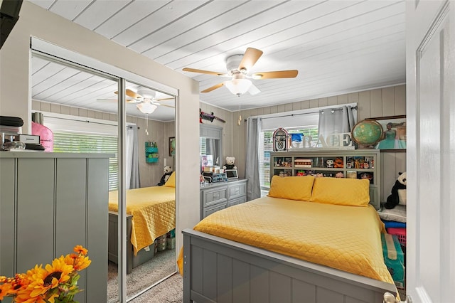 carpeted bedroom featuring ceiling fan and wood walls