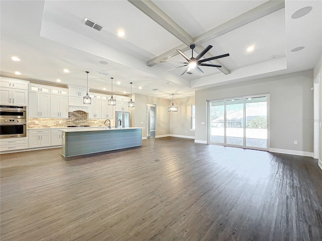 unfurnished living room featuring a raised ceiling, ceiling fan, dark wood-type flooring, sink, and beamed ceiling
