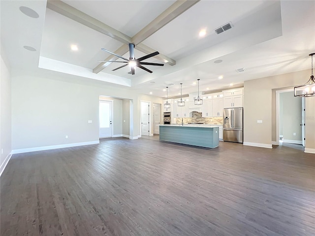 unfurnished living room with beam ceiling, dark hardwood / wood-style floors, ceiling fan, and a tray ceiling
