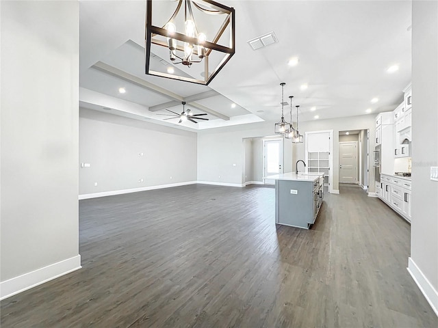 kitchen featuring dark wood-type flooring, sink, white cabinetry, hanging light fixtures, and an island with sink