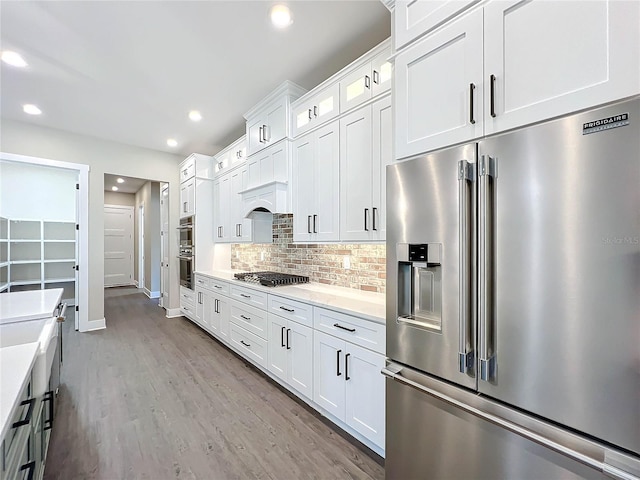 kitchen featuring premium range hood, light hardwood / wood-style floors, decorative backsplash, white cabinets, and appliances with stainless steel finishes