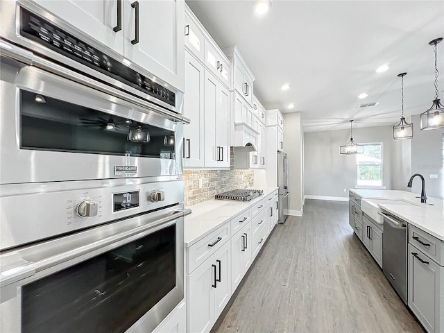 kitchen featuring pendant lighting, backsplash, white cabinets, light wood-type flooring, and appliances with stainless steel finishes